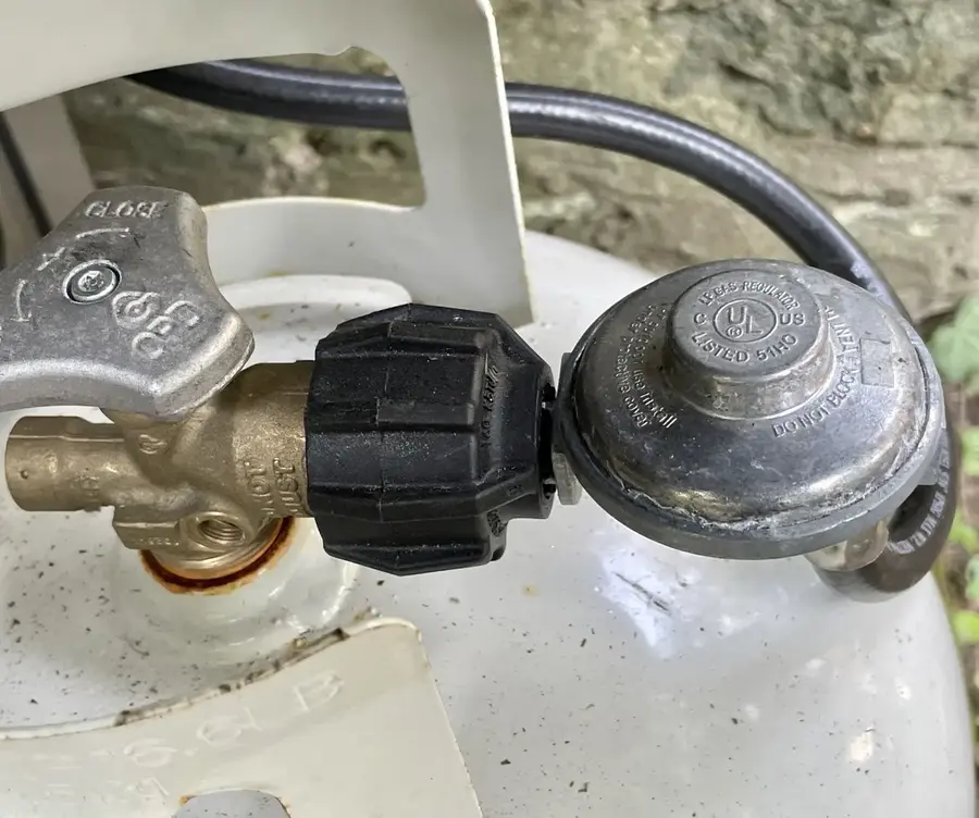 A black Type 1 QCC1 handwheel connecting a grill regulator to a propane cylinder
